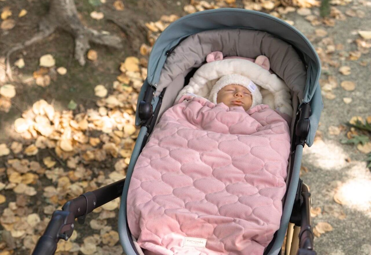 a baby in a sleeping bag in a stroller on a walk