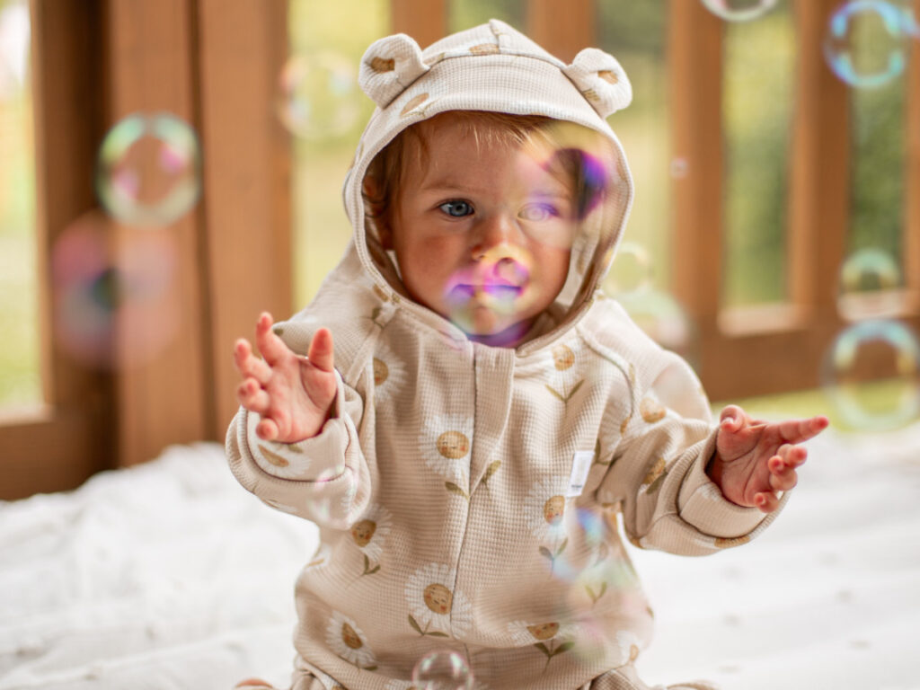 dziecko w kombinezonie łapie bańki mydlane